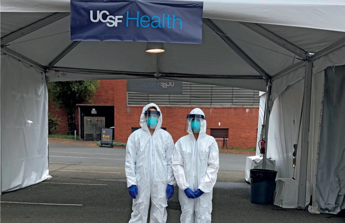 Two healthcare workers in protective gear at a UCSF Health tent.