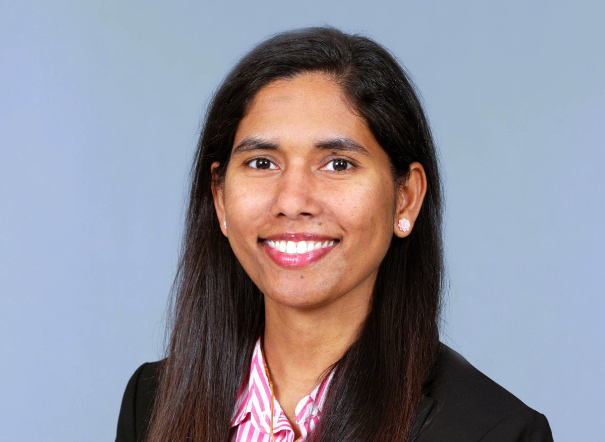 A woman smiling in professional attire against a light blue background.