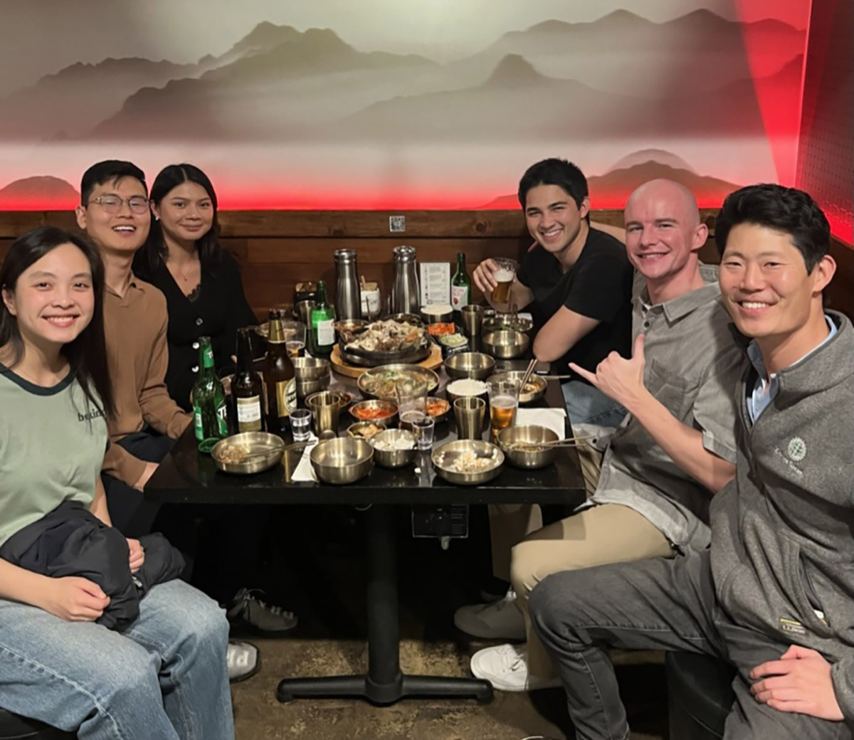 A group of seven people dining together at a table filled with food and drinks.