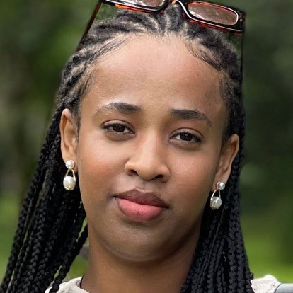 A woman with braided hair and pearl earrings, outdoors.