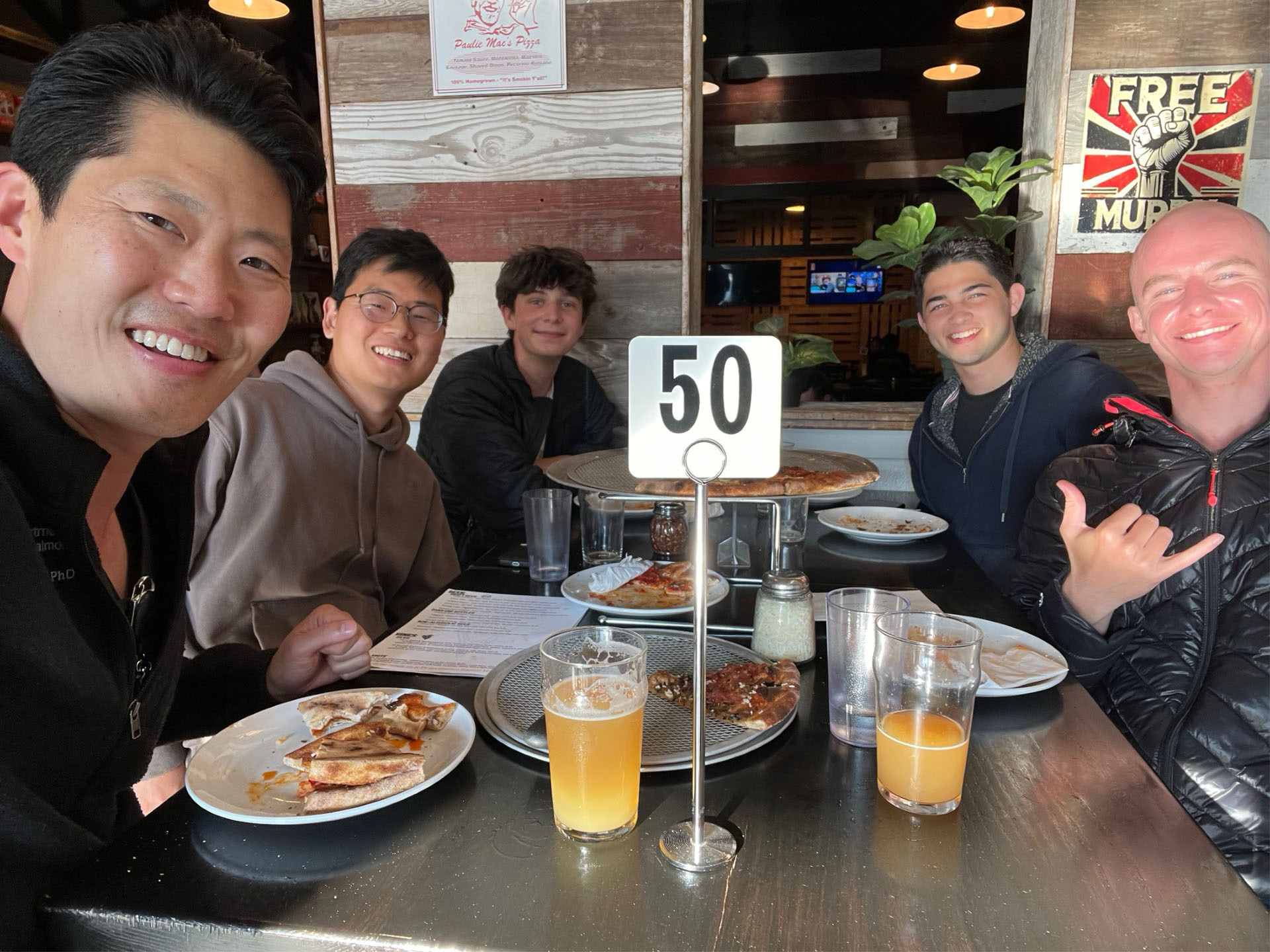 Five friends at a restaurant table with food and drinks.