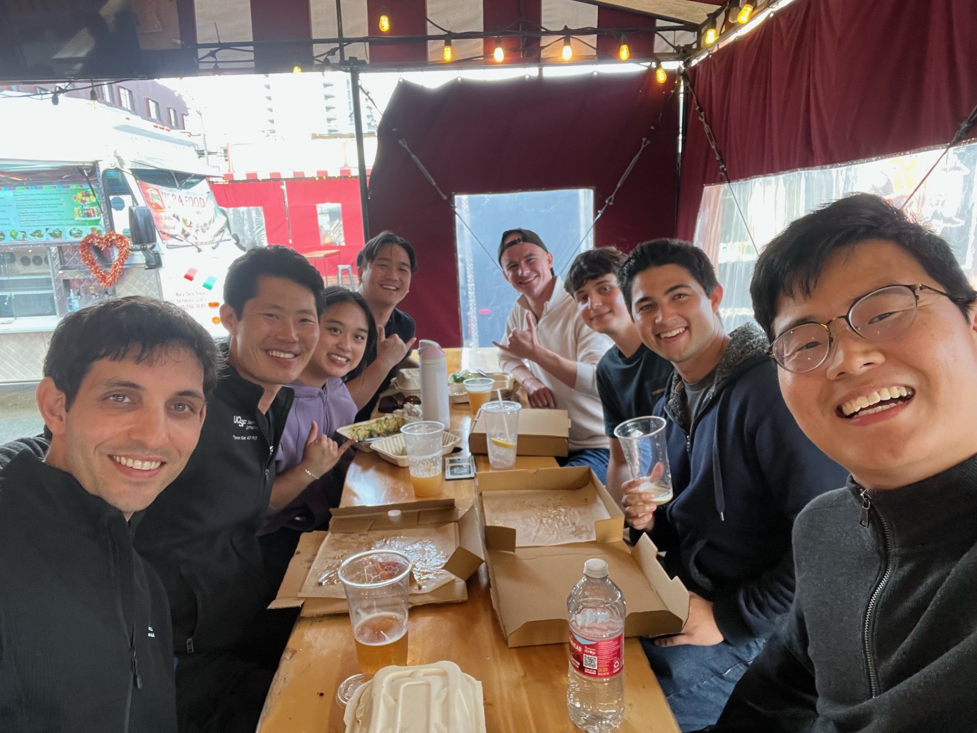 A group of eight friends smiling while eating together at a table.
