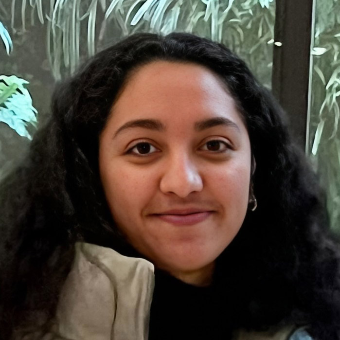 A person with curly hair smiling in front of greenery. Ou Lab Research People UCSF Yvonne.