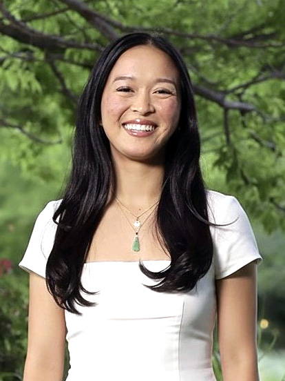 A woman smiling outdoors with long dark hair.