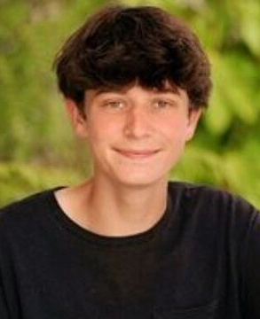 A young man smiling against a blurred green background.