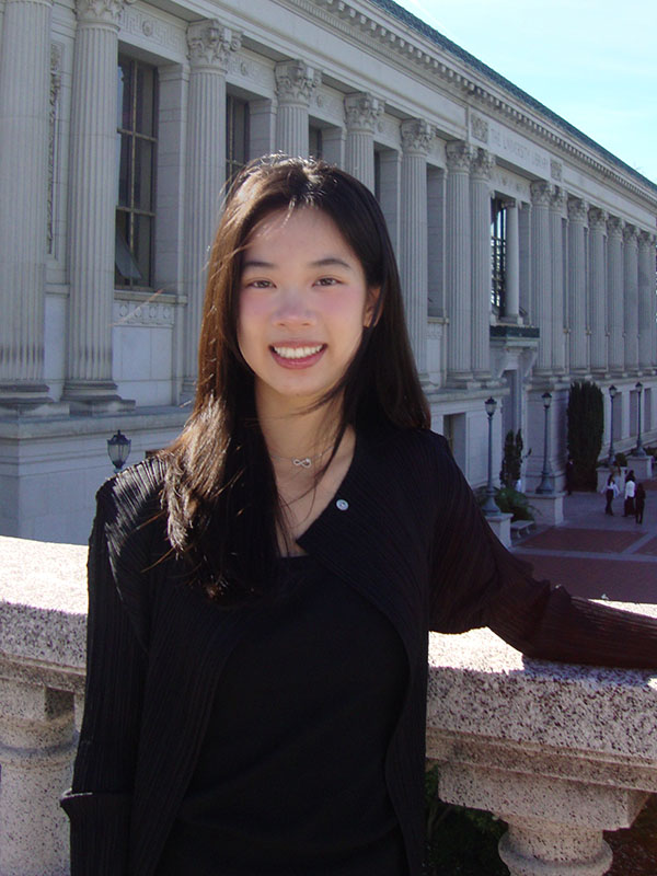 A woman smiling outdoors near a historic building.