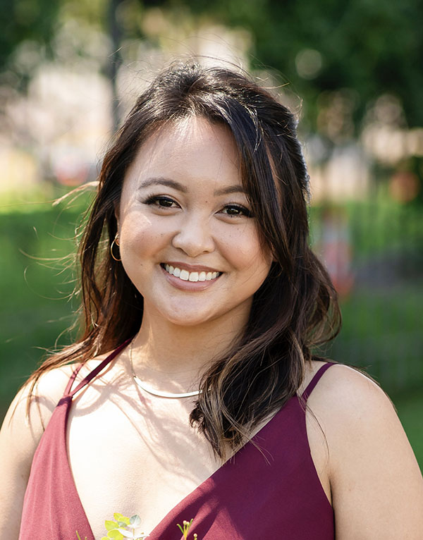 A woman smiling outdoors in a burgundy dress.
