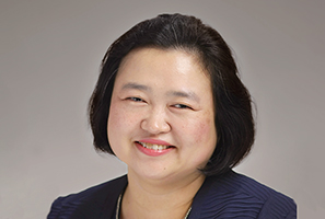 A woman smiling with dark hair and a black blazer against a neutral background.